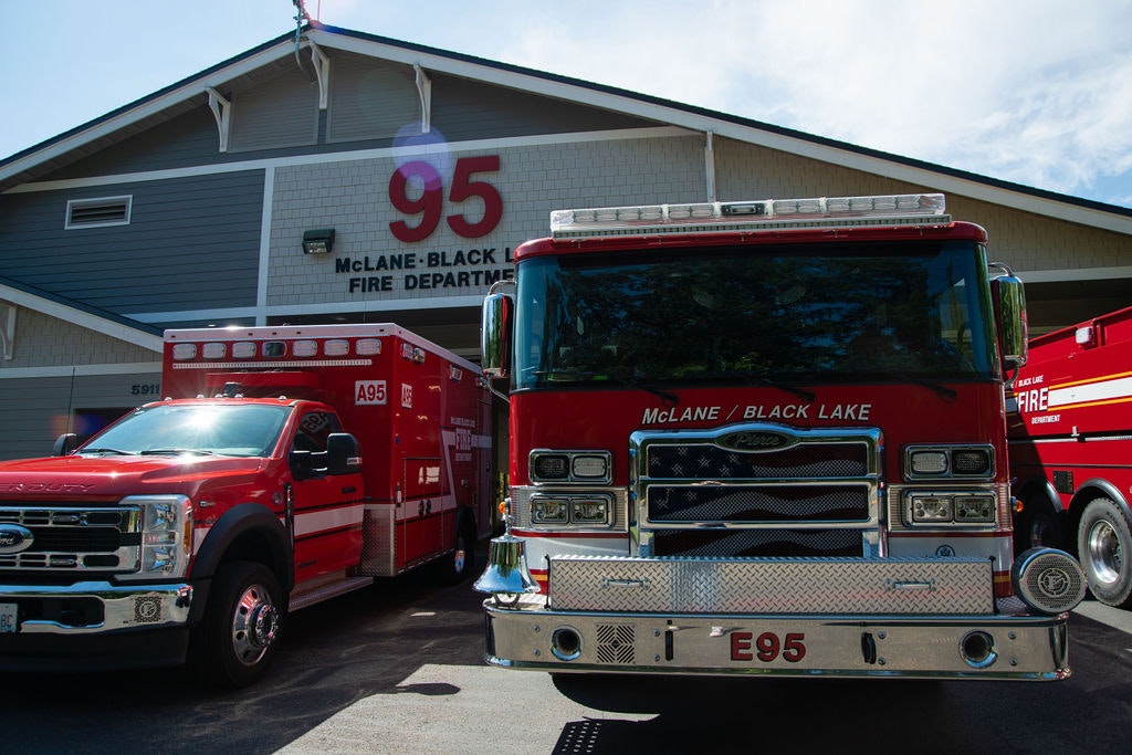 The image shows a fire department featuring a red fire truck and an emergency vehicle outside a building.
