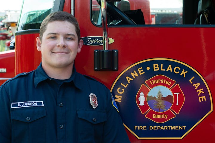 A firefighter stands next to a fire truck with the McLane Black Lake Fire Department logo.