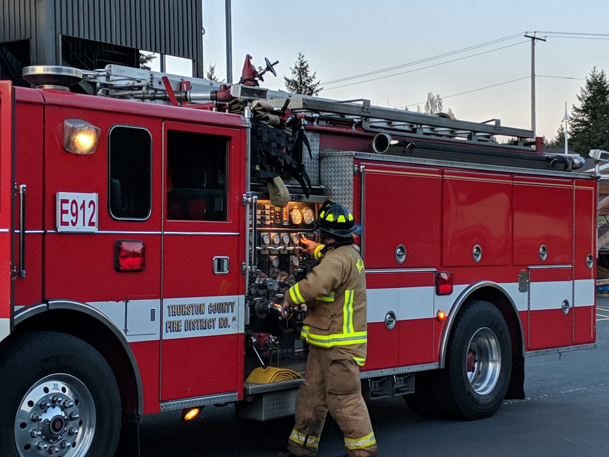 Firefighter in gear working on a red fire truck labeled "E912" in an outdoor setting.