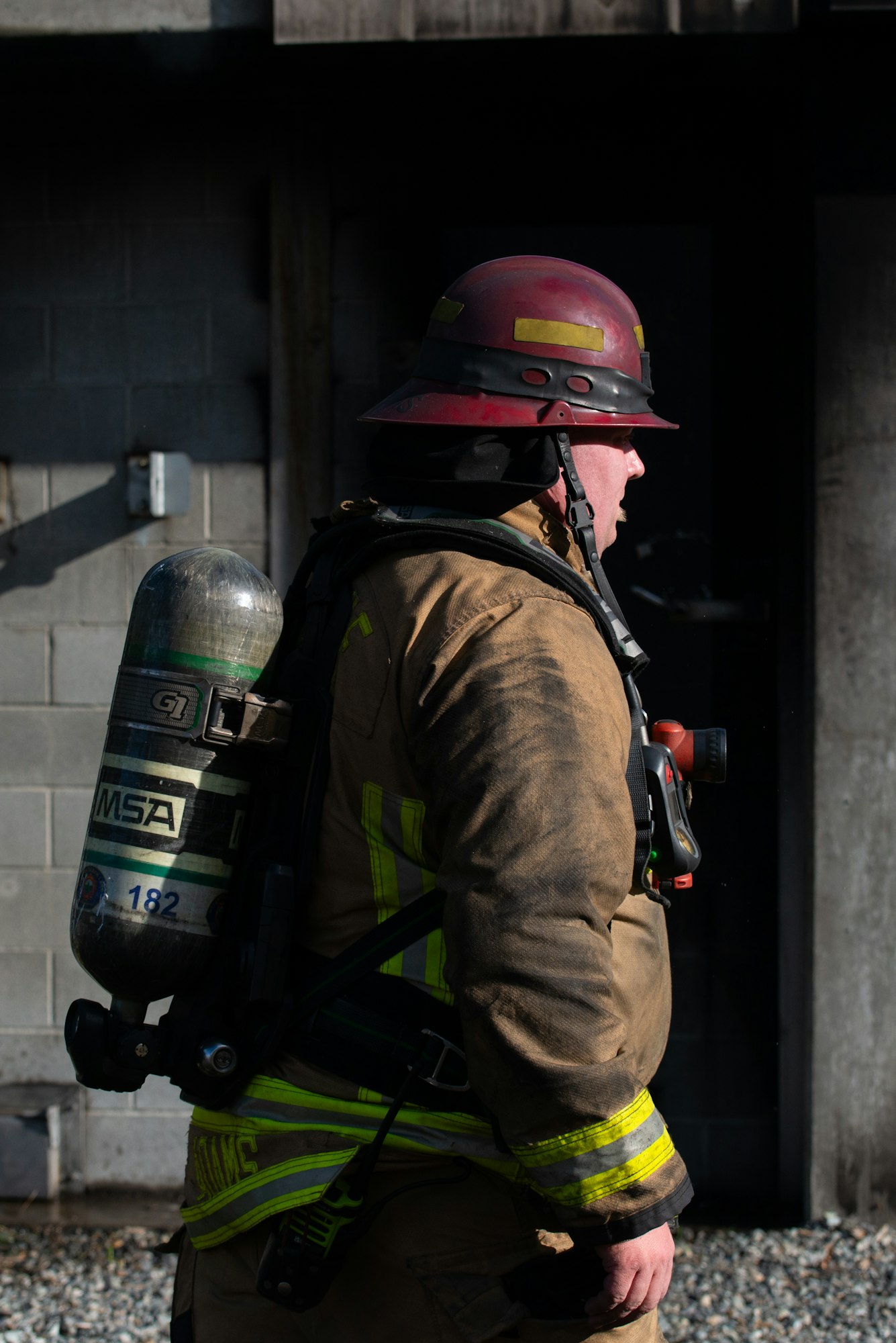 A firefighter in gear, wearing a helmet and air tank, stands outside a building, prepared for action.