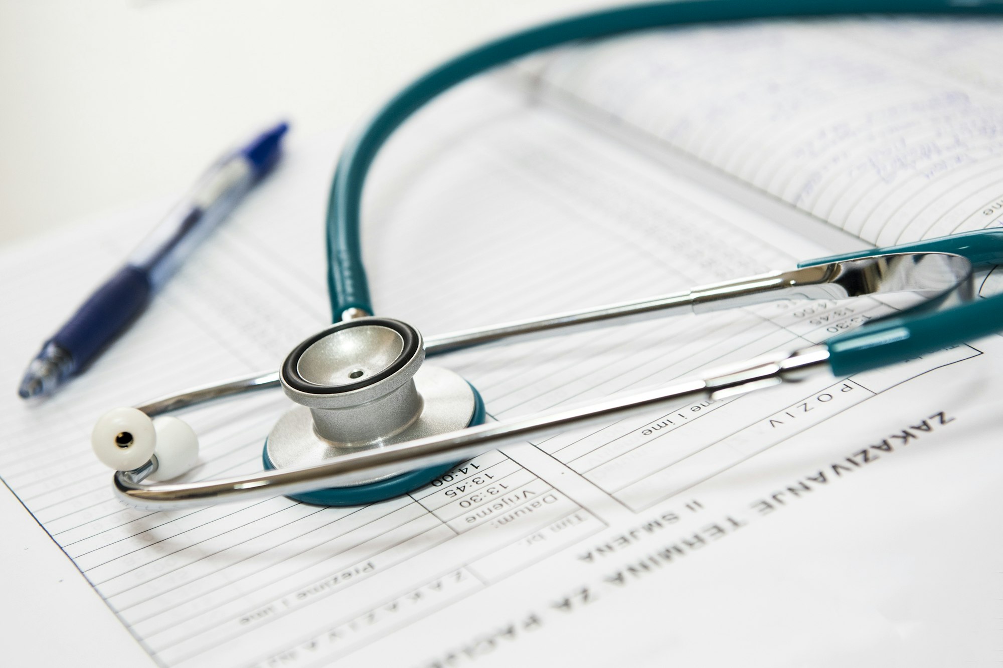 The image features a stethoscope resting on medical forms, accompanied by a blue pen, suggesting a healthcare setting.