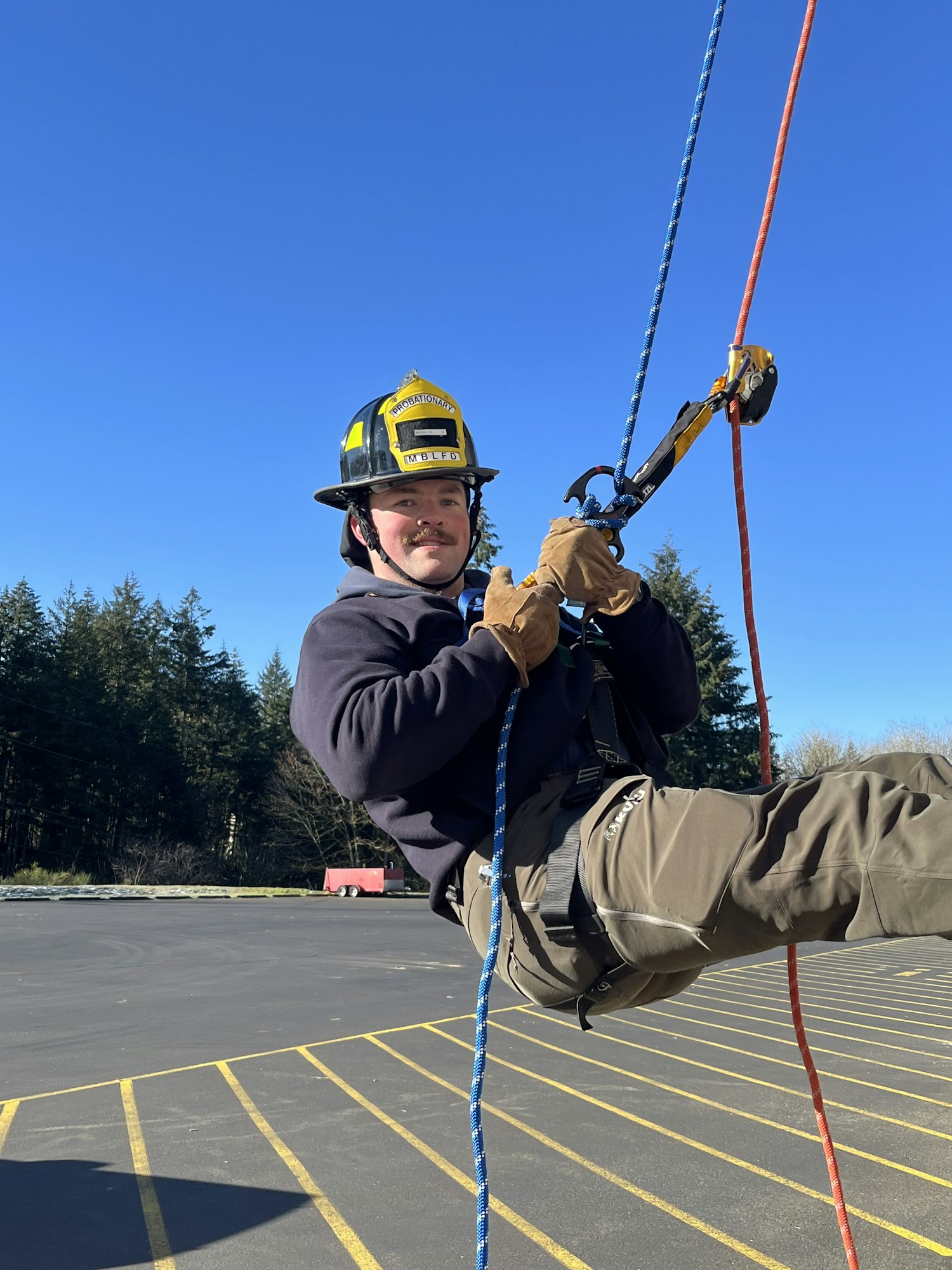 A person in a helmet is rappelling down using ropes, demonstrating climbing or rescue techniques outdoors under a clear sky.