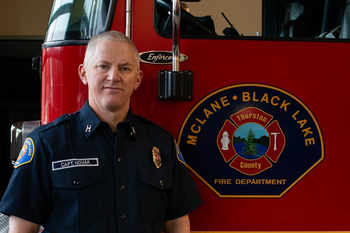 A firefighter, identified as Capt. Novak, stands next to a fire truck with the McLane Black Lake Fire Department emblem.