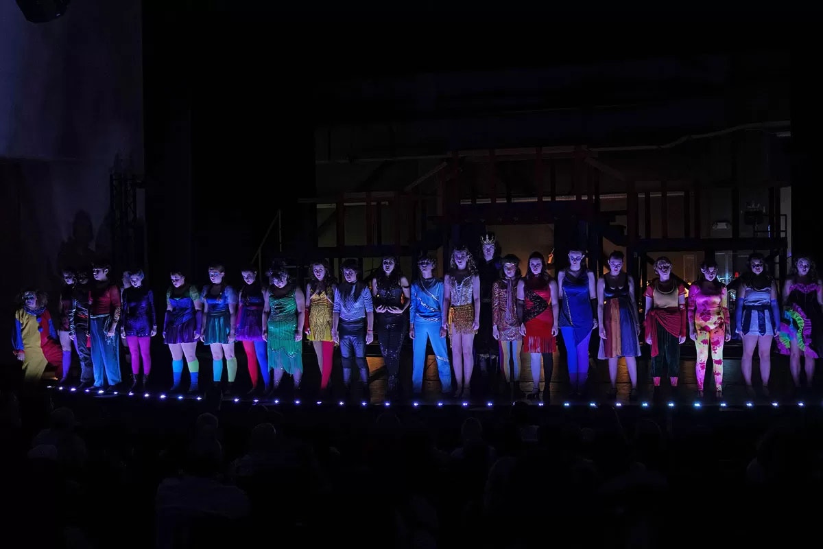 A group of people on stage in colorful costumes under dim lighting.