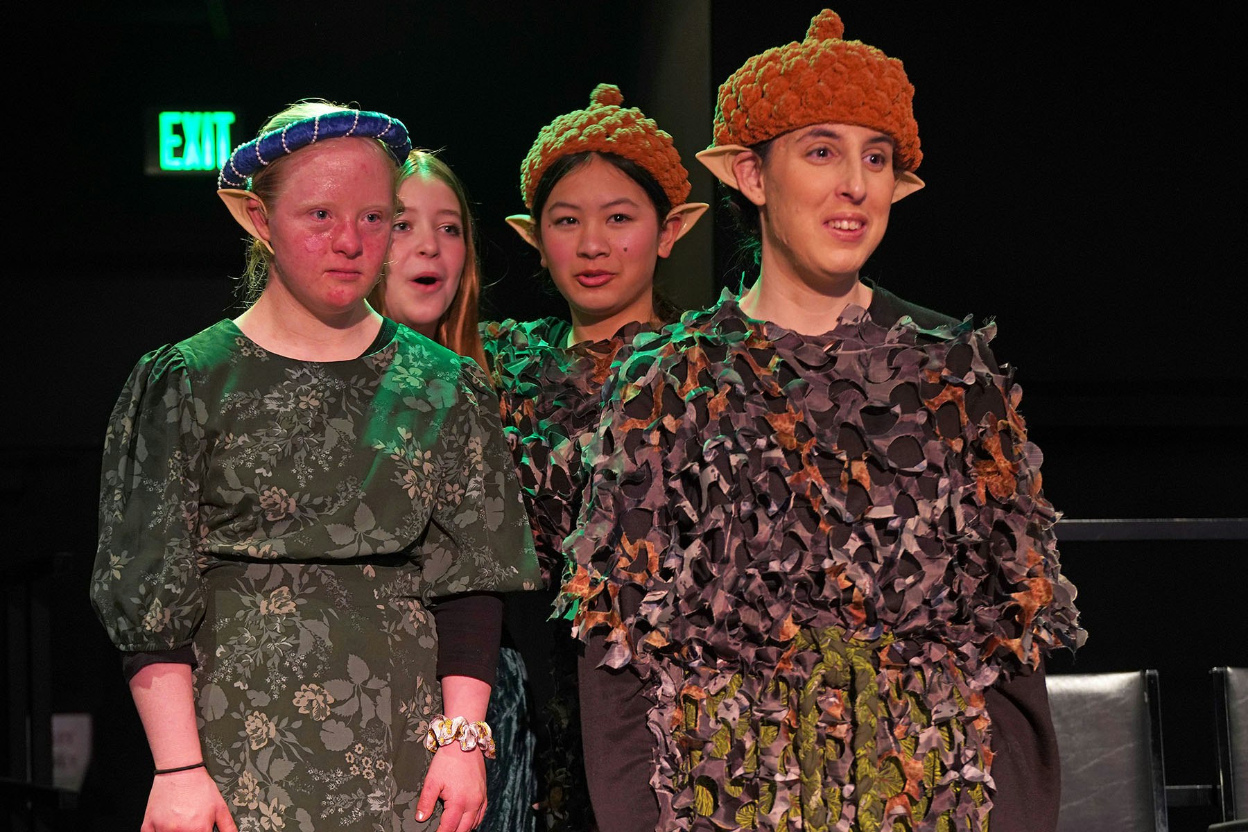 People in costume with elf-like ears and textured outfits, appearing on stage.