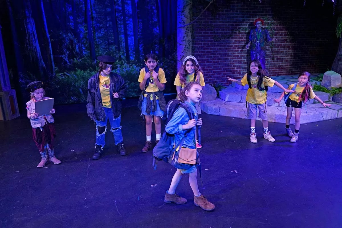 Children in costume on a stage resembling a forest, performing a play or musical.