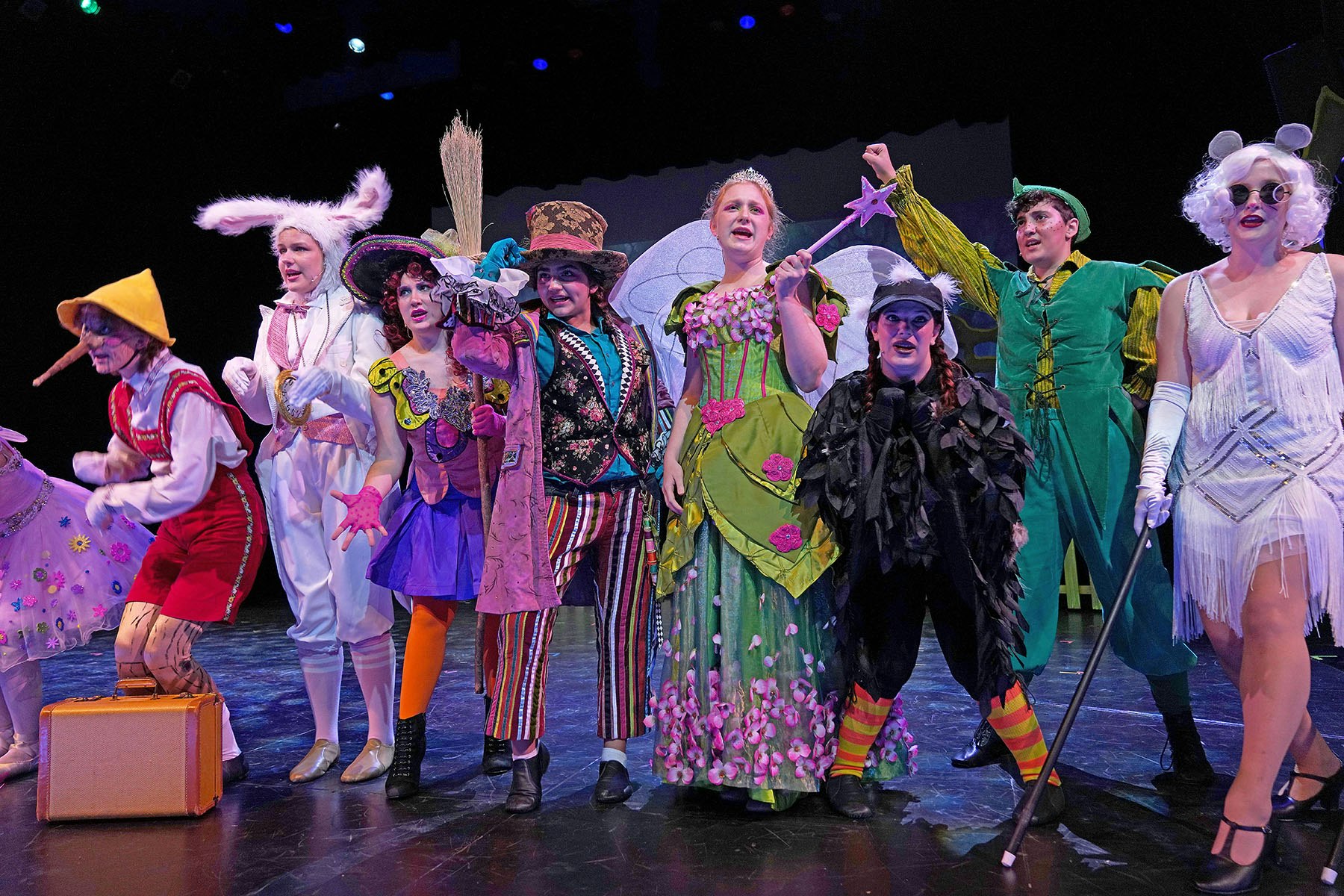A group of performers in colorful, fairy tale-themed costumes on stage, striking poses.