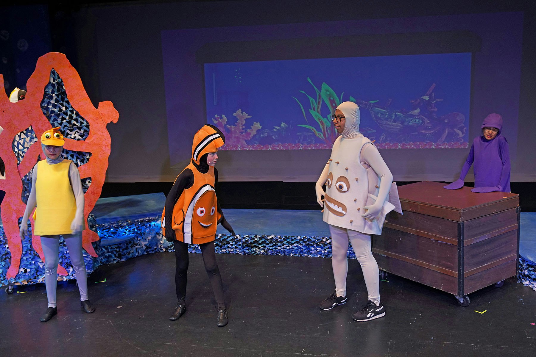People in colorful aquatic-themed costumes performing a play on stage.