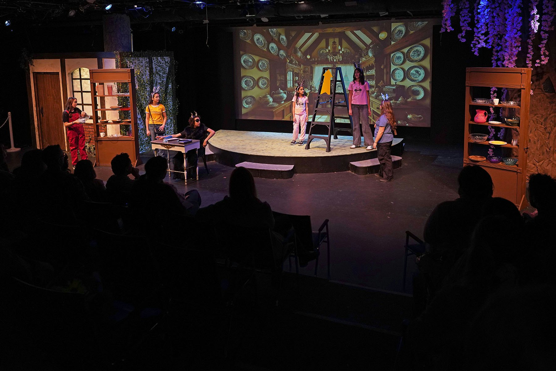 A theatrical performance with cast members on stage, some in costumes, and an audience watching.