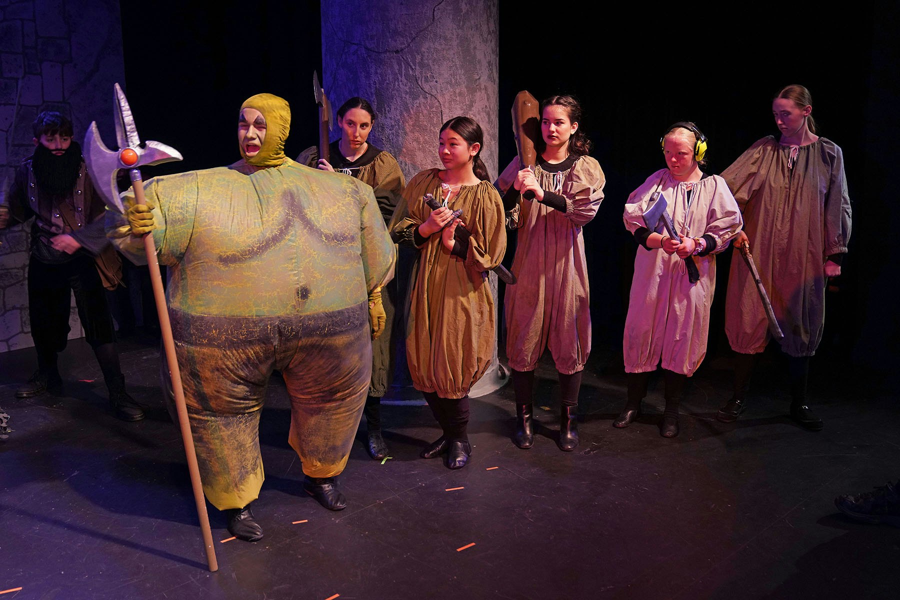 A group of people in medieval-style costumes holding various props on stage.