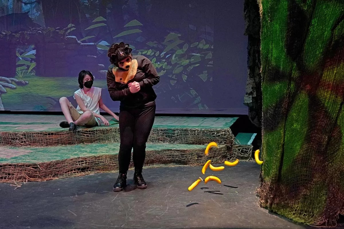 Two people in costume on a stage with jungle scenery and CGI yellow snakes.