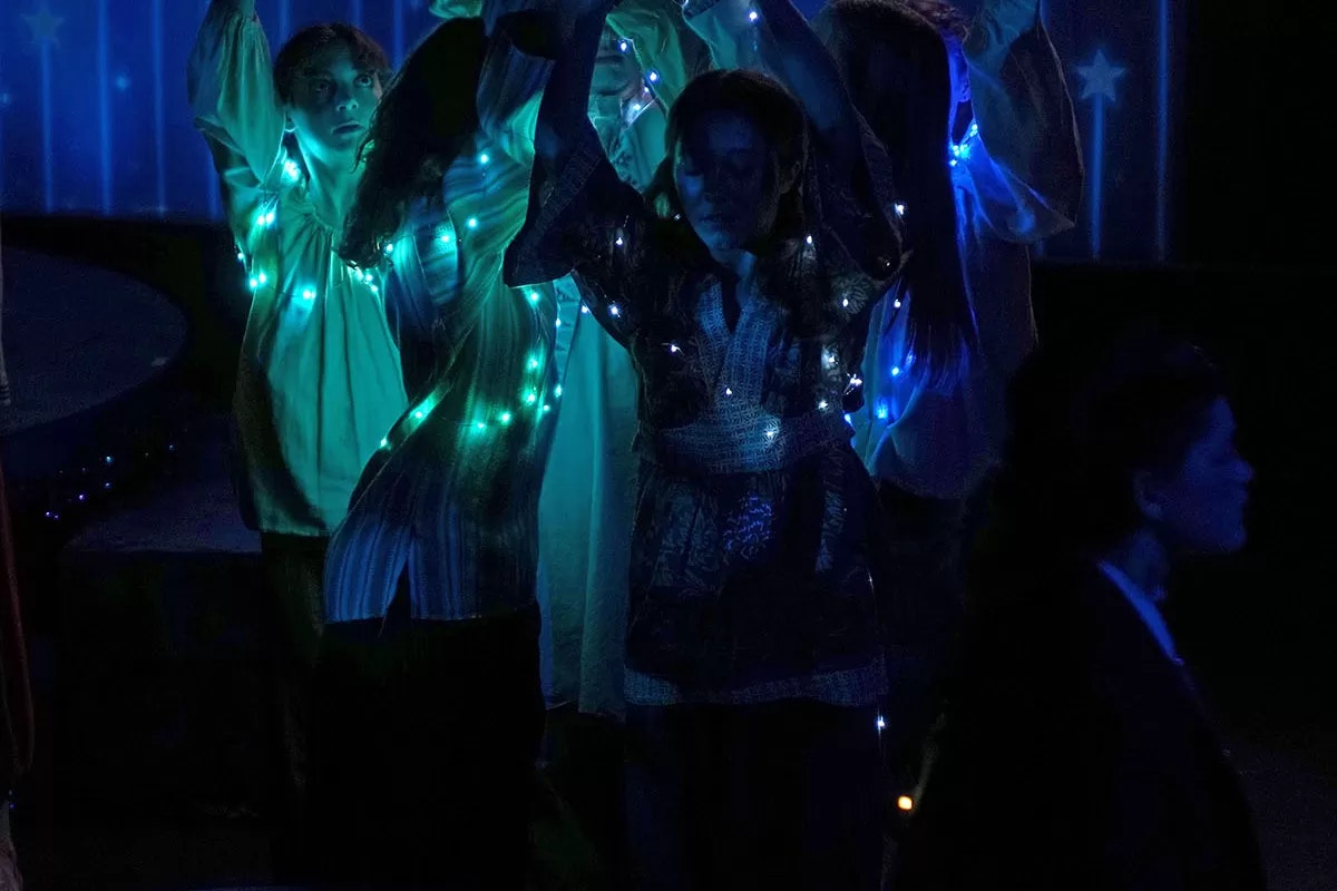 People in dark attire illuminated by blue and green lights.