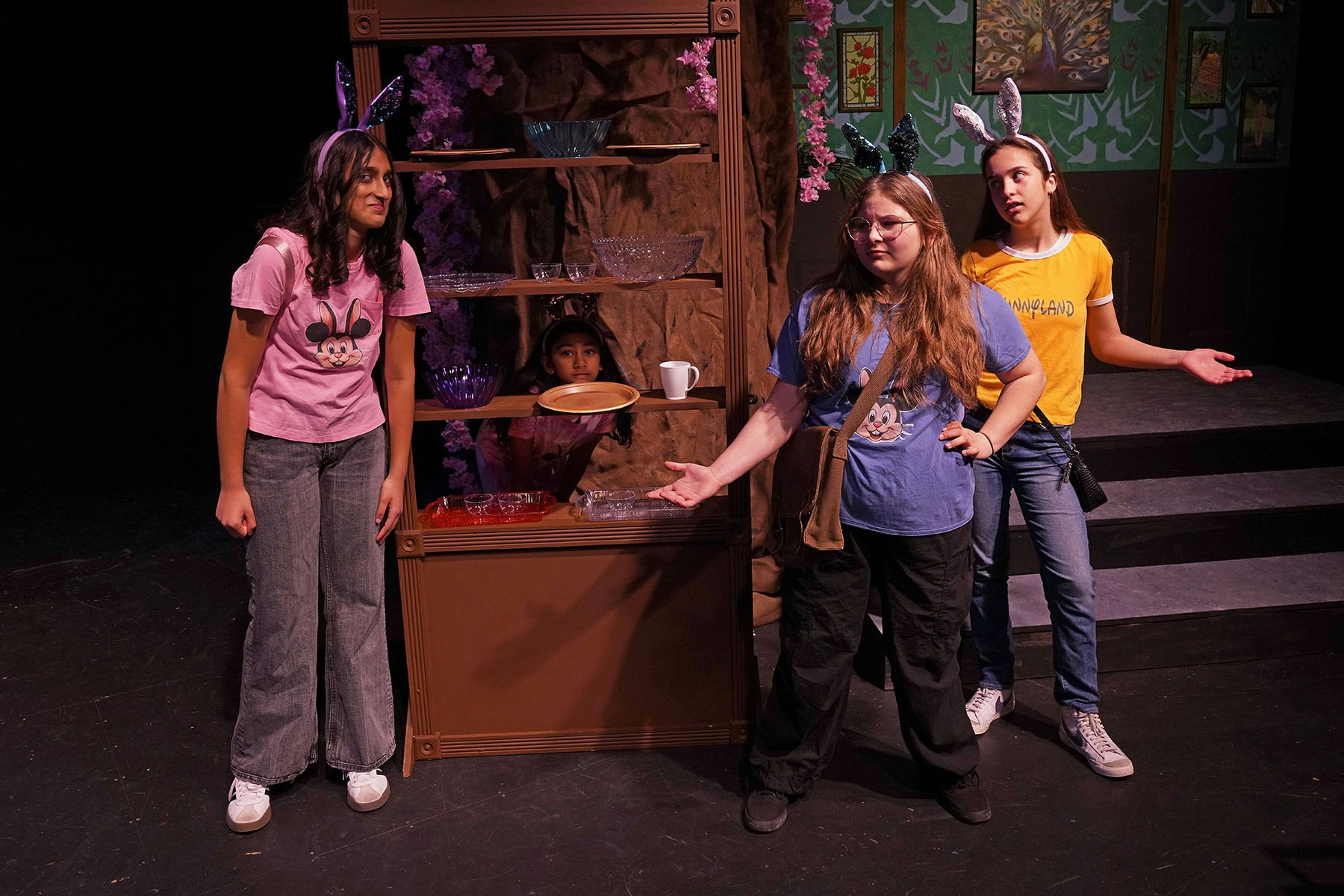 Four people with bunny ears and casual clothes on stage, standing around a shelf with dishes.