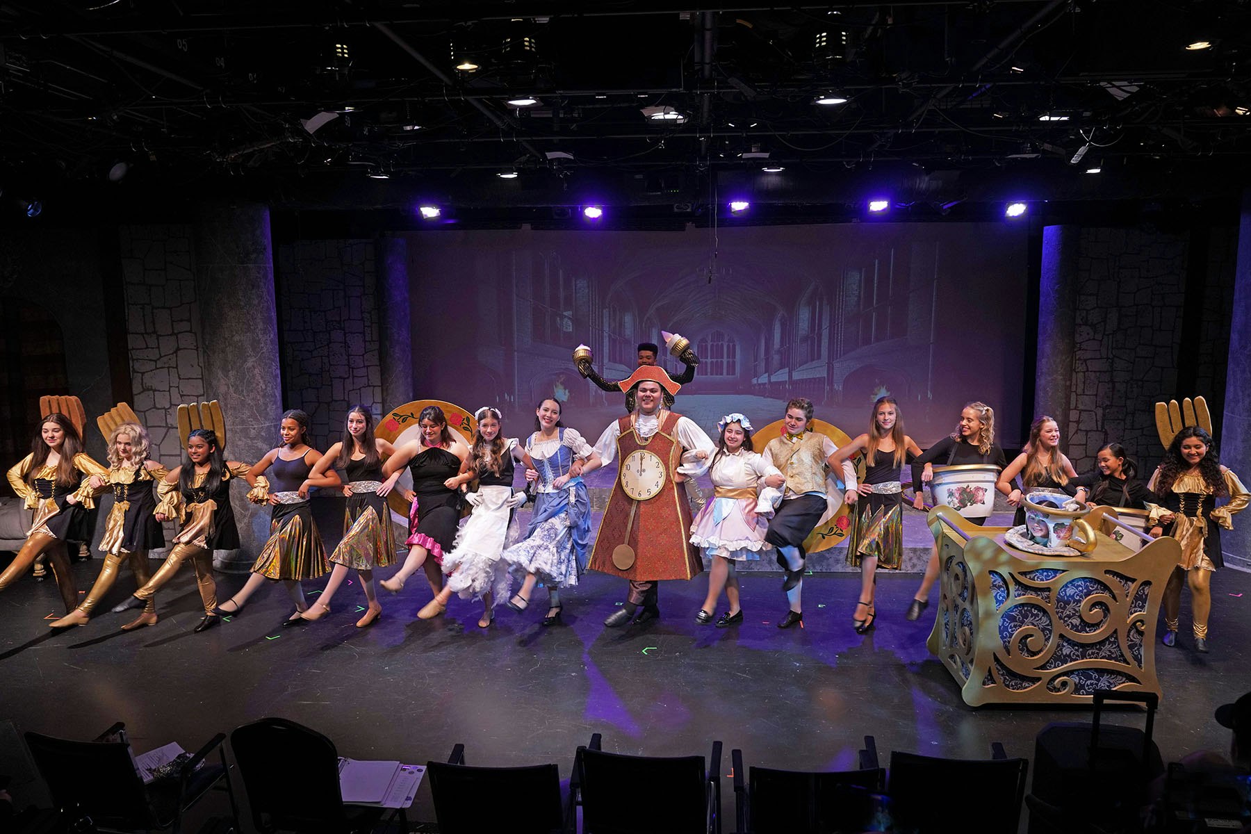 Performers on stage in costume, possibly a musical, with lively dance and colorful set designs.
