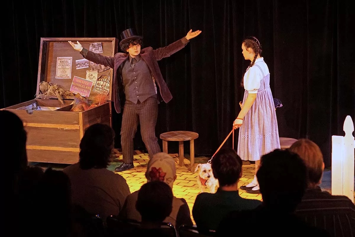 Two people performing on stage, one with a dog on a leash, in front of an audience.