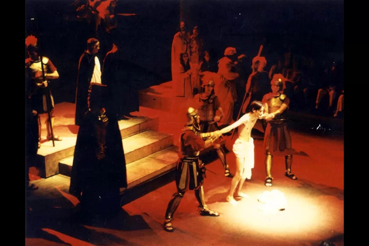 A theatrical scene depicting a historical setting, likely from Roman times, with a man in white surrounded by soldiers.