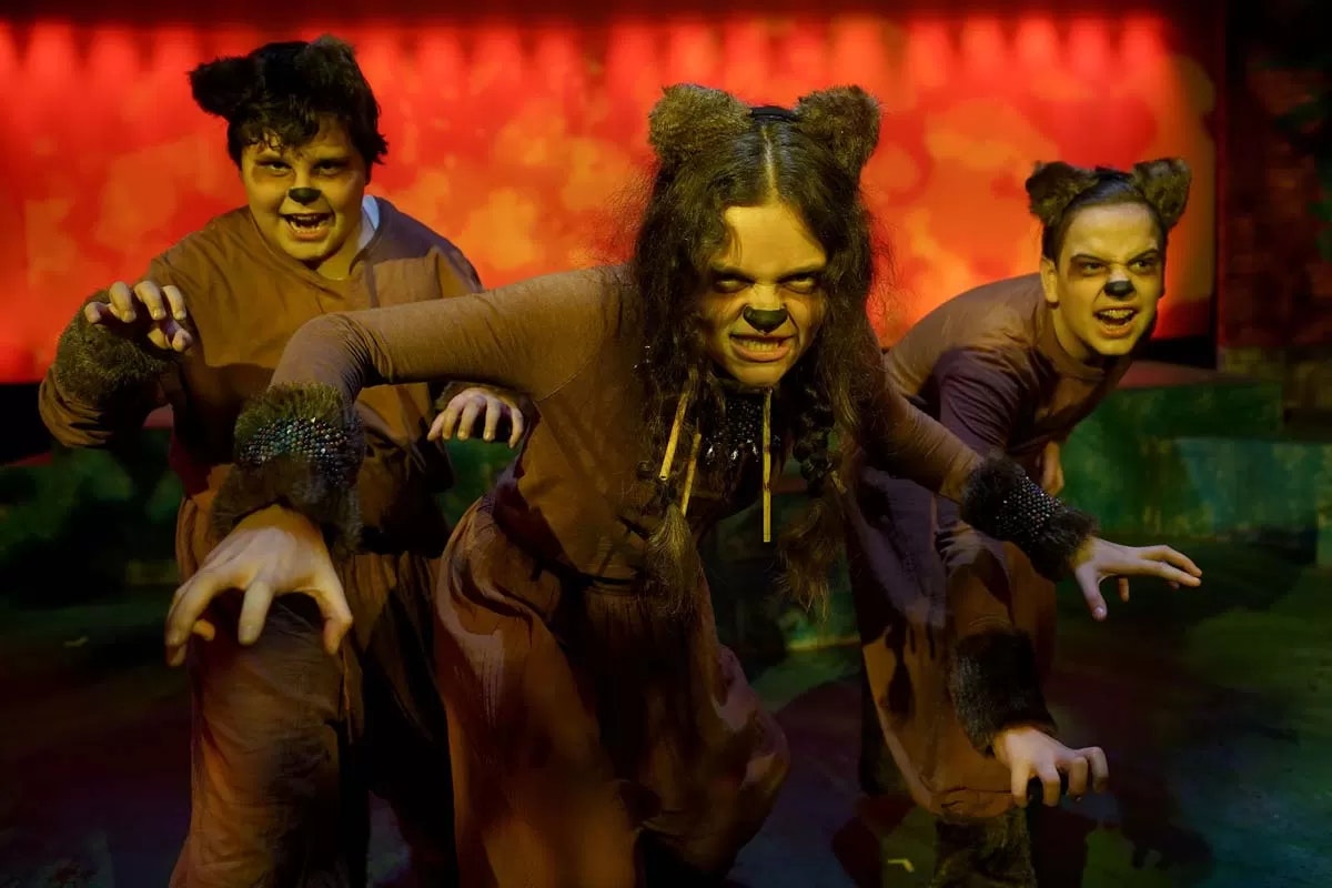Three people in bear costumes making fierce expressions, set against an orange background.