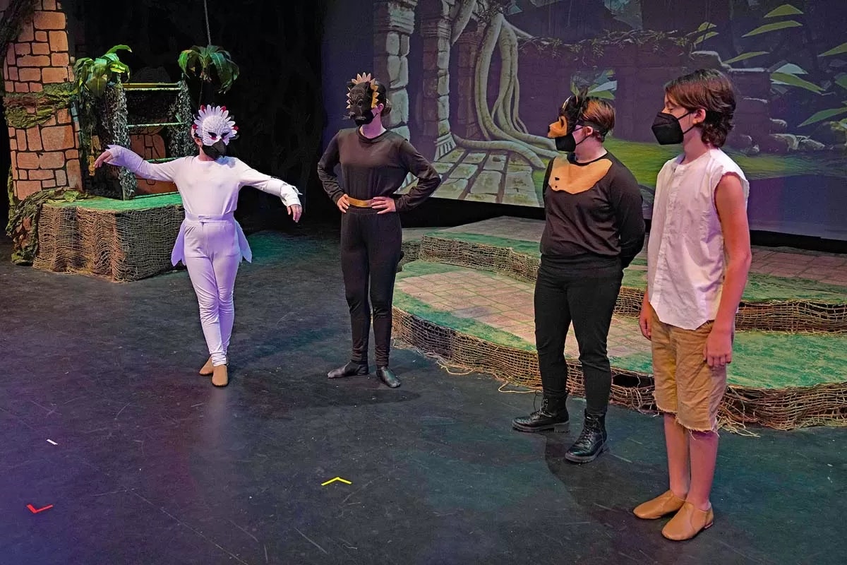 Four people in costumes and masks perform on a stage with a jungle-themed backdrop.