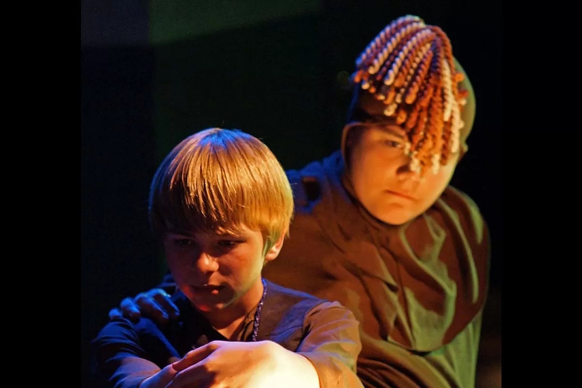 Two people in dramatic lighting, one with a serious expression, the other wearing a headpiece with beaded strands.