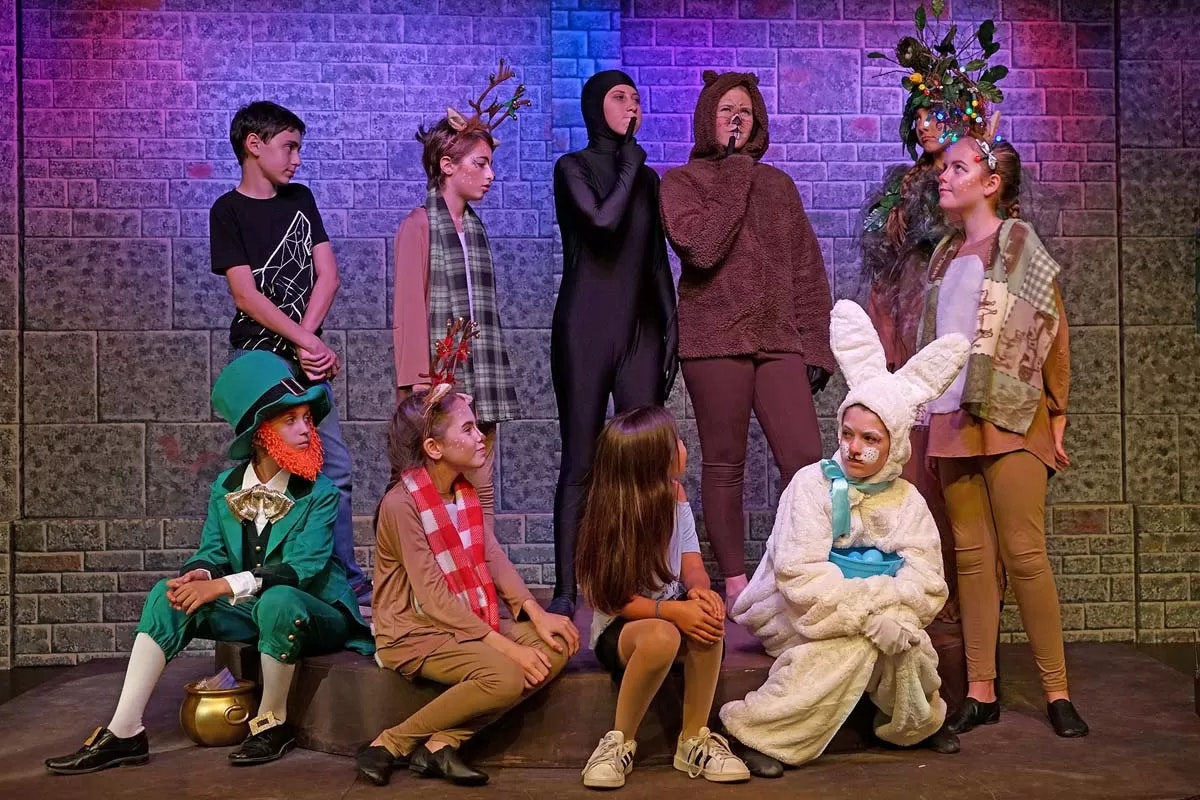 A group of people in animal and fantasy costumes on stage, including a bear, rabbit, deer, and an elf.