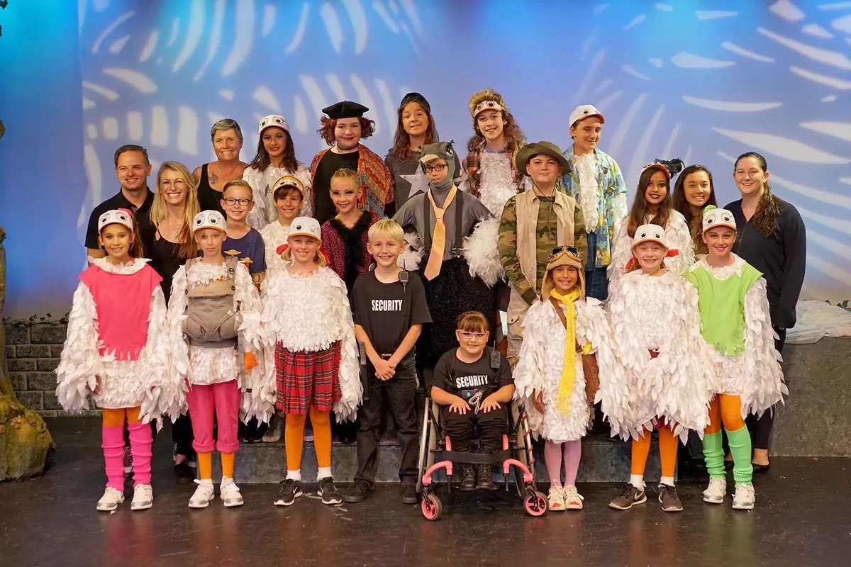 A group of children and adults in costumes on stage, posing for a photo.