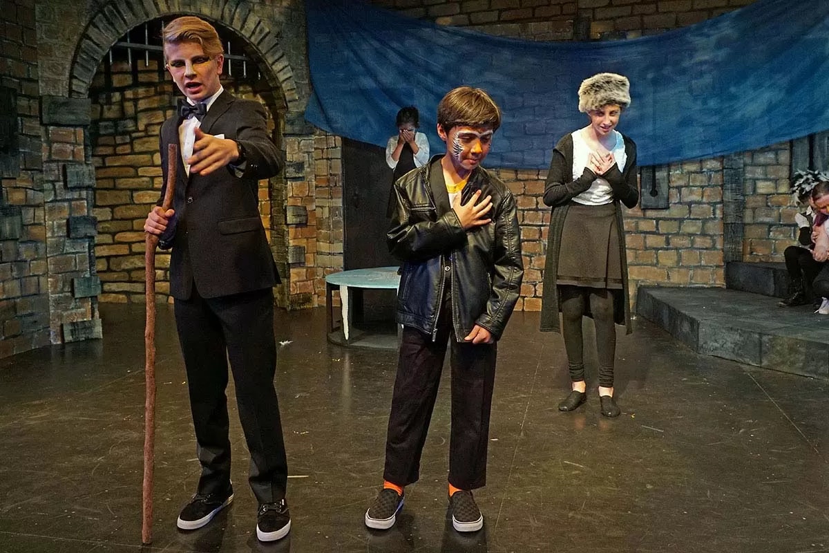Children in costume perform on stage with a brick backdrop.
