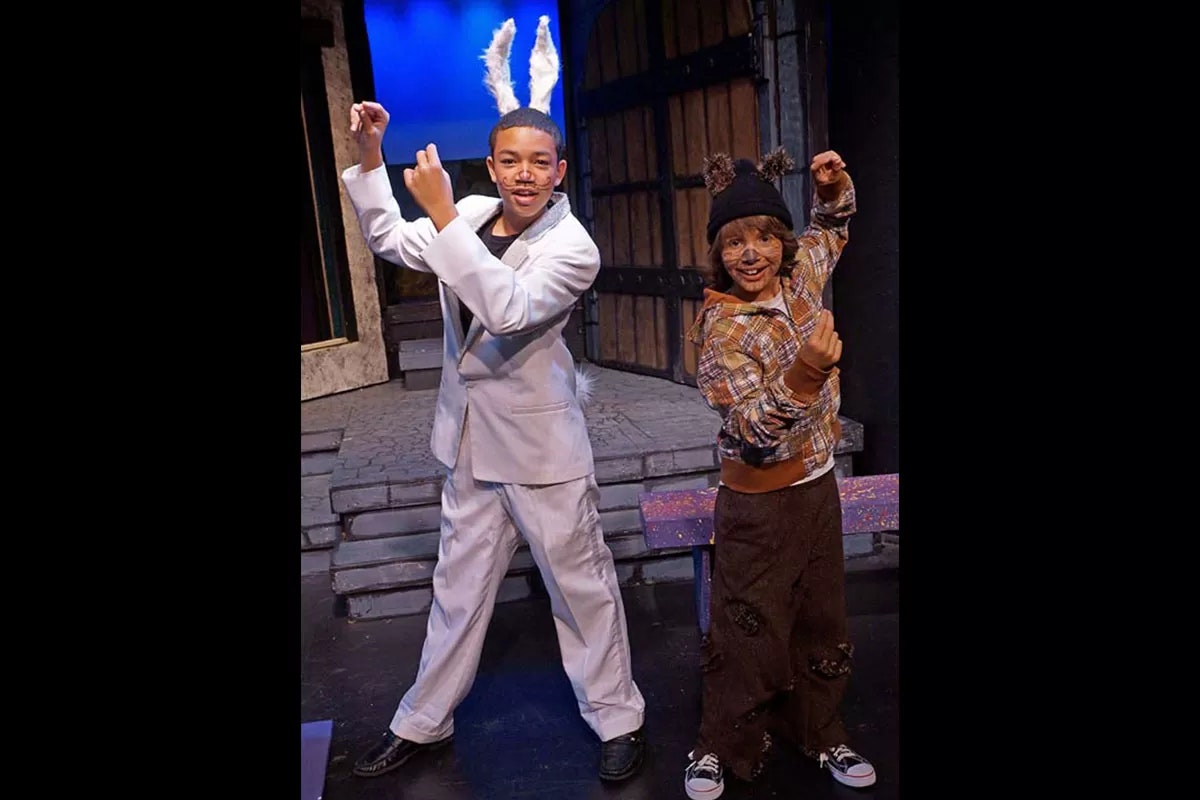 Two people are in costume on stage, one with bunny ears and the other with bear ears, posing and smiling.