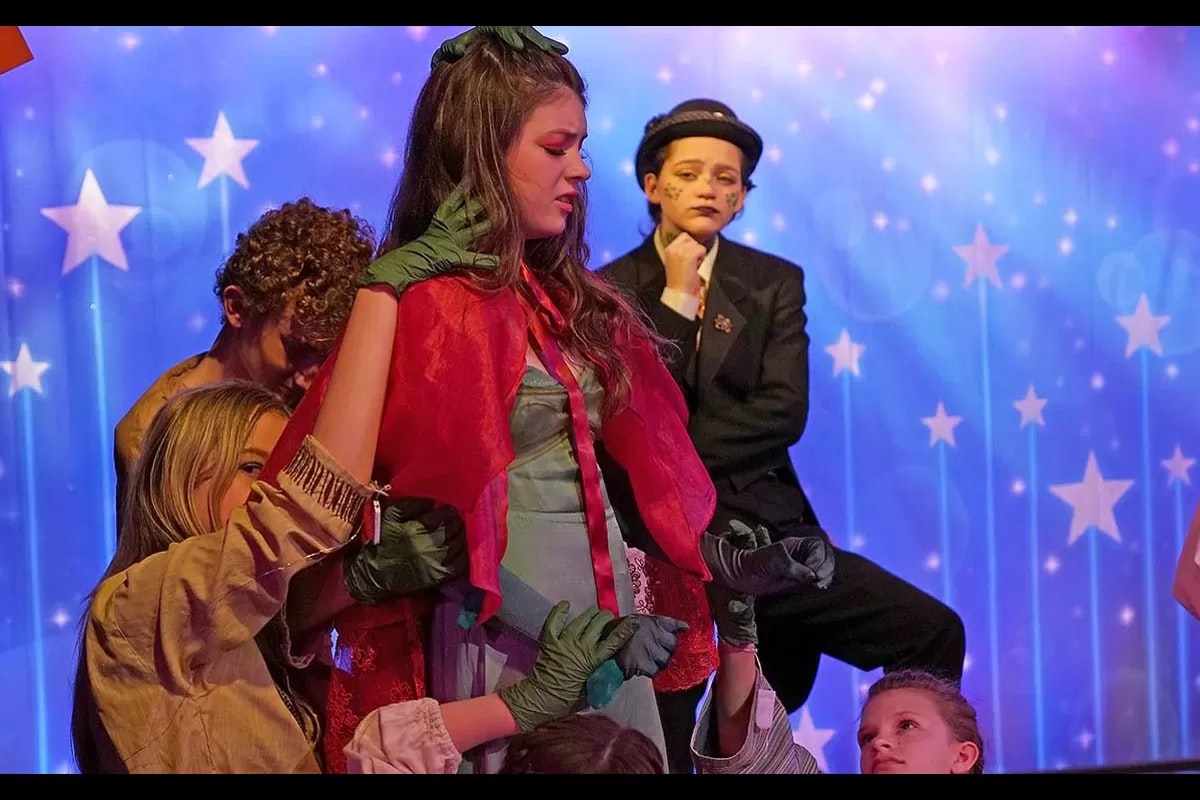 A theatrical scene with performers in colorful costumes and makeup, in front of a starry blue backdrop.