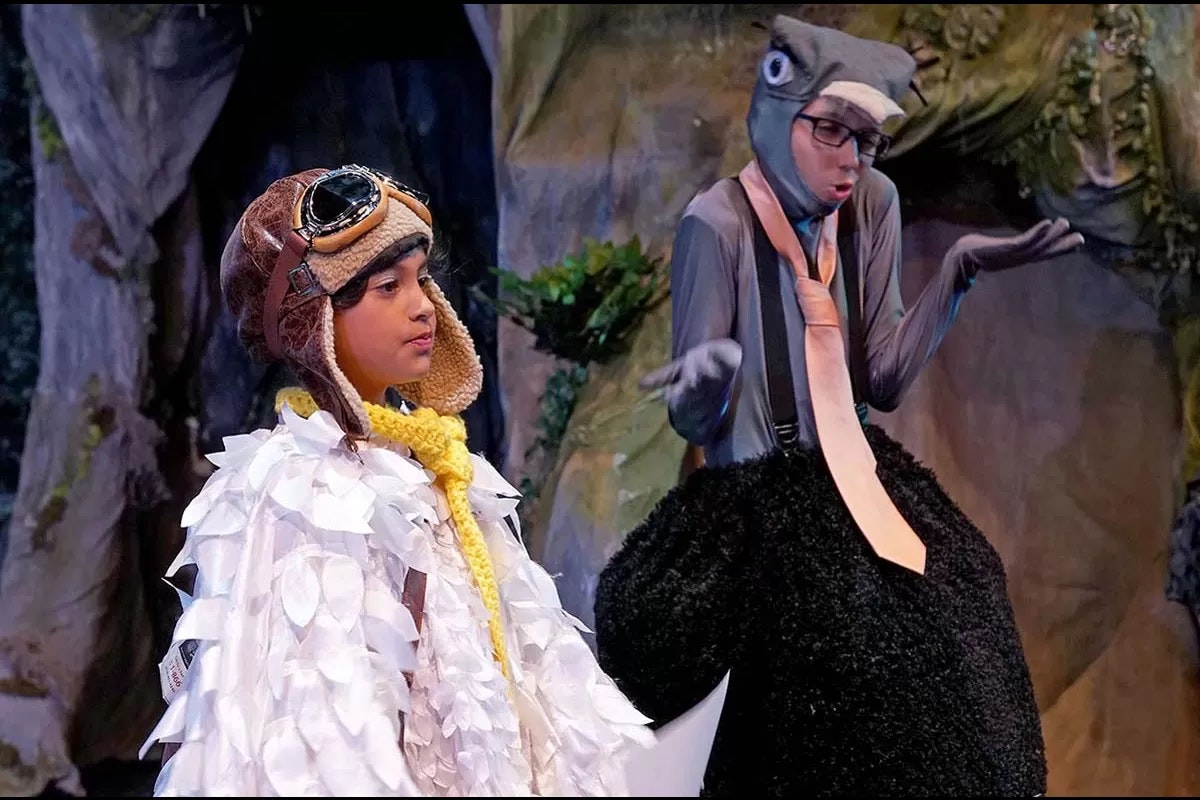 Two people in costume on stage; one in a bird outfit with goggles, the other in a grey animal suit with buck teeth and a tie.