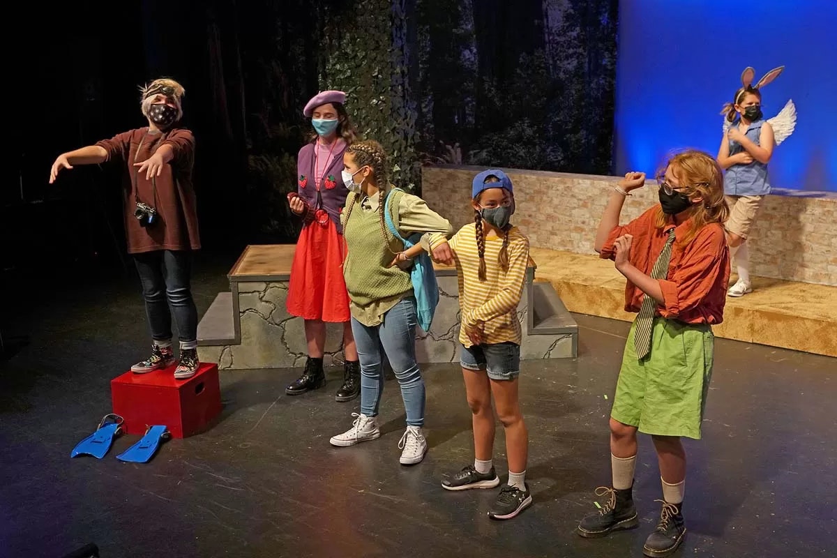 People on stage in colorful costumes, wearing masks, performing in a play.