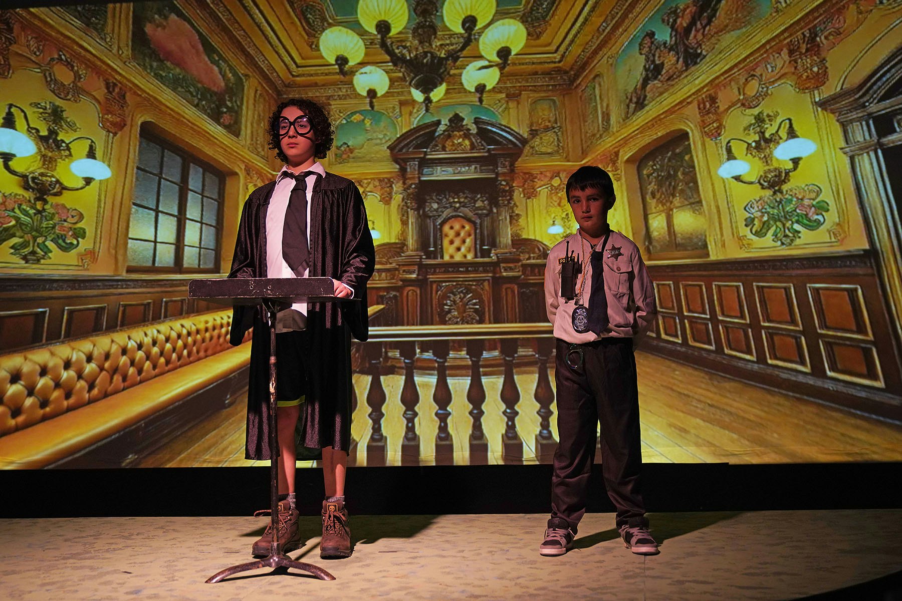 Two boys dressed as judge and policeman in a courtroom setting.