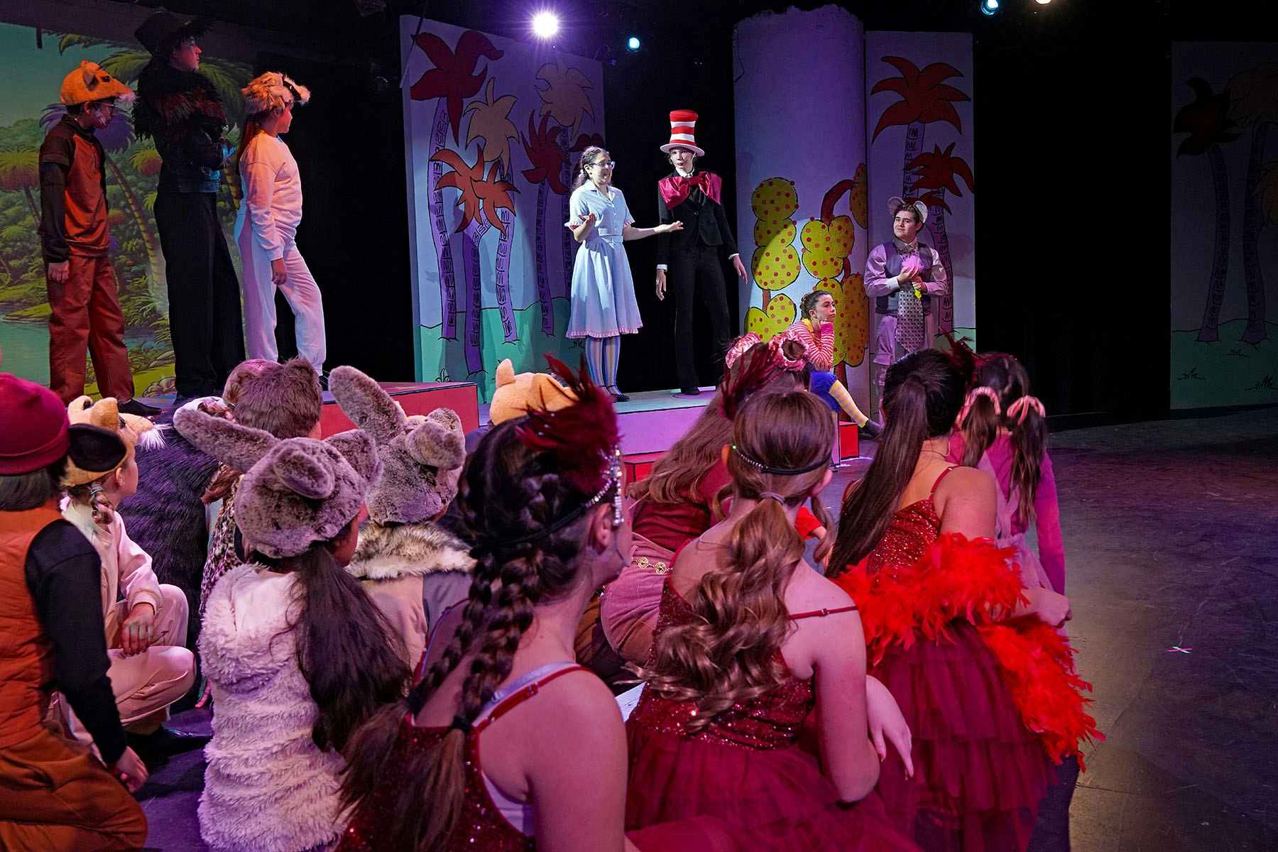 A vibrant theater scene showcasing a performance with children in costumes, singing and dancing on stage.