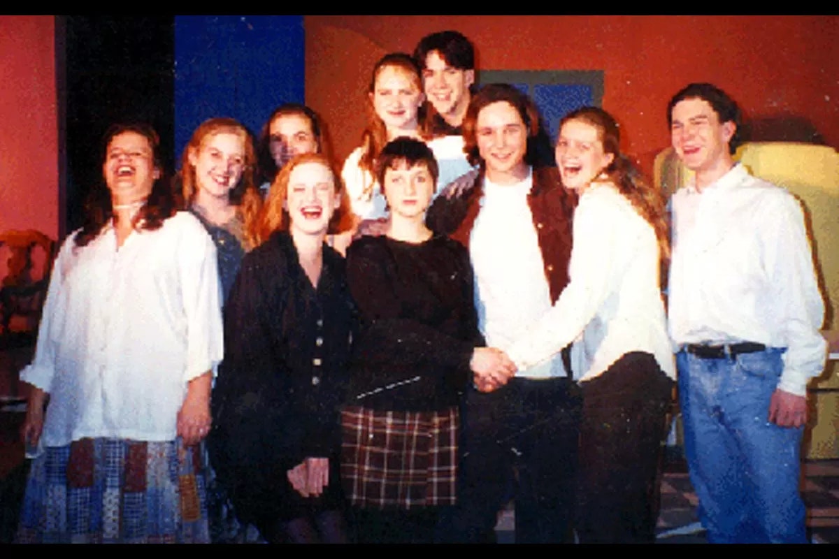 A group of people smiling for a photo, standing together in a casual, indoor setting.