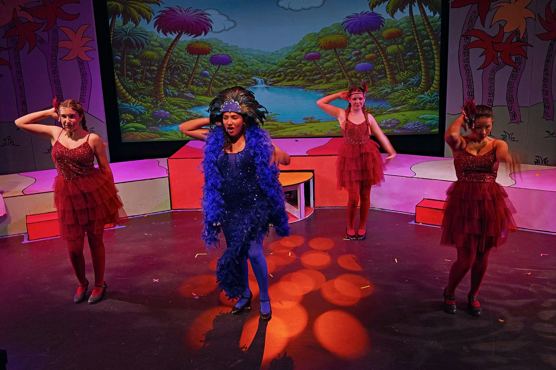 A vibrant stage performance with dancers in sparkly outfits and colorful backgrounds, showcasing lively choreography.