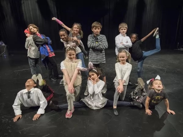 A group of children posing on stage, some doing splits, others striking various playful poses.