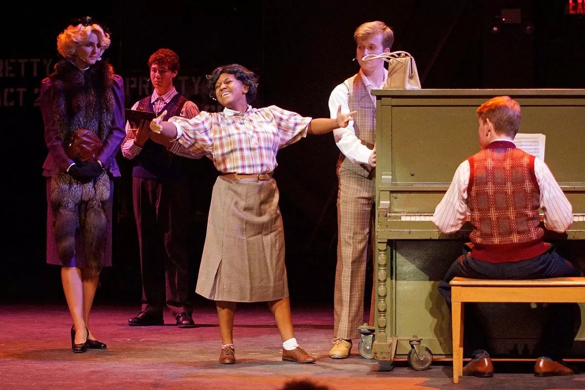 A musical performance scene with a woman singing, a pianist, and three people watching attentively on stage.