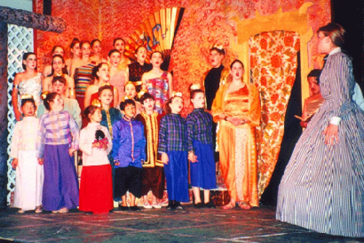 A group of people in colorful costumes performing on stage in front of a decorative backdrop.