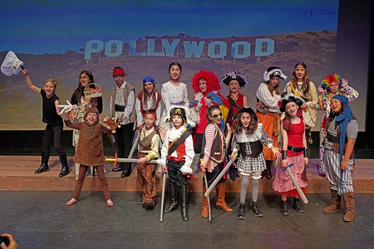 Children in costumes pose on stage with a backdrop reading "POLLYWOOD."