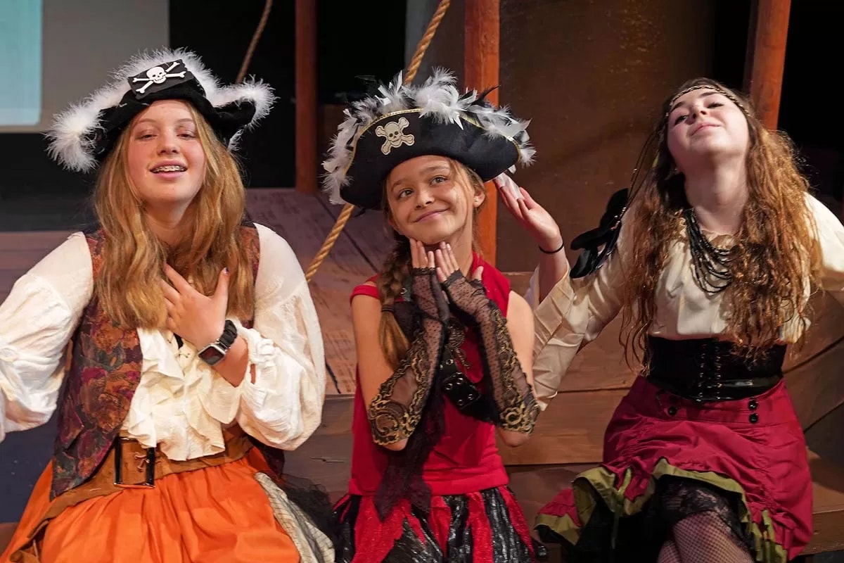 Three people in pirate costumes posing playfully on a stage setting.