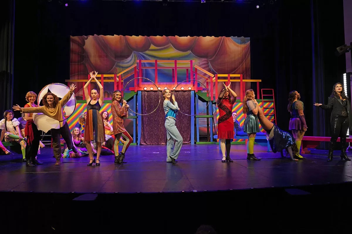 A colorful stage performance with people in vibrant costumes and a whimsical set design.