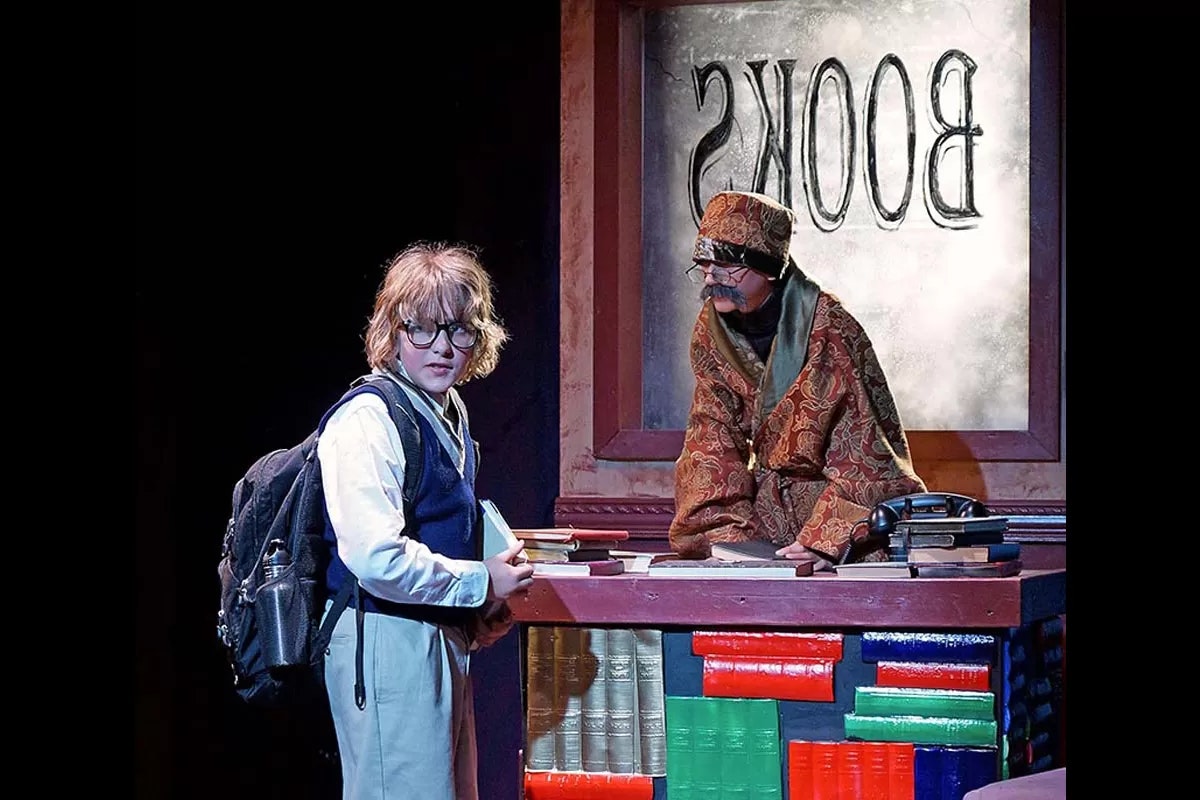 A young person with glasses and a backpack, and an older person behind a desk with "BOOKS" seen in reverse on a window.