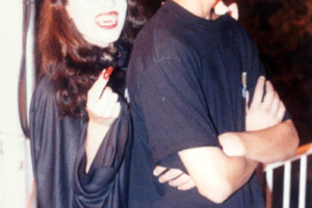 Two people standing back-to-back, one in a vampire costume with a playful expression.