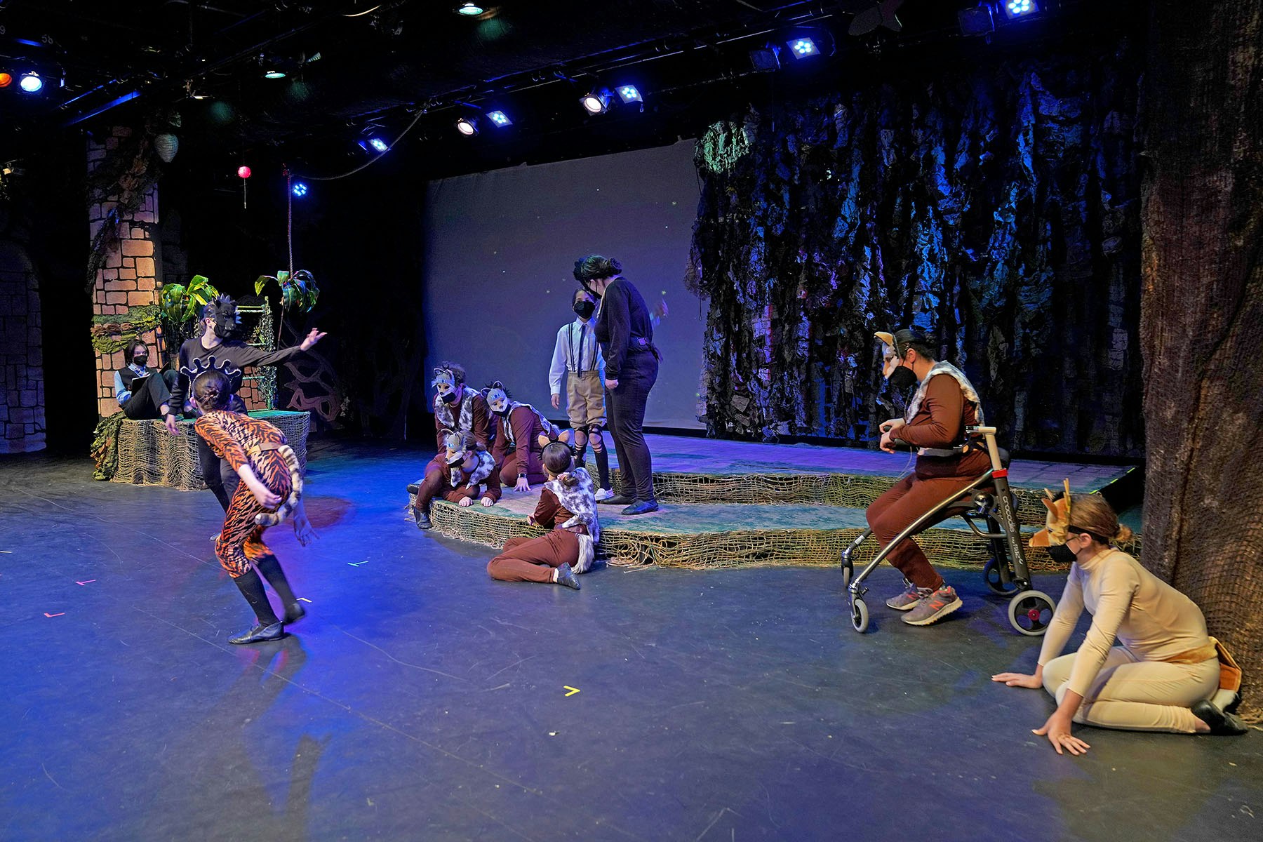 A stage performance with people in animal costumes, set in a forest-like environment.