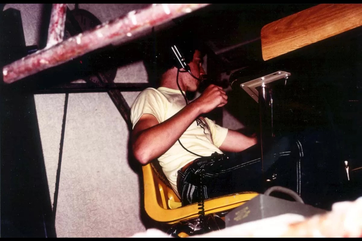 A person wearing a headset, sitting in a yellow chair, appears to be in a work setting, possibly at a control panel.