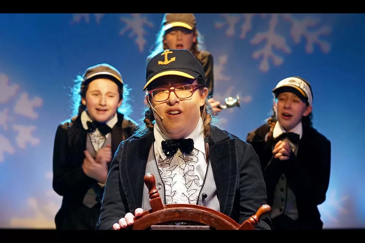 A group of people wearing matching costumes and hats, with one holding a ship's wheel, set against a snowy-themed backdrop.