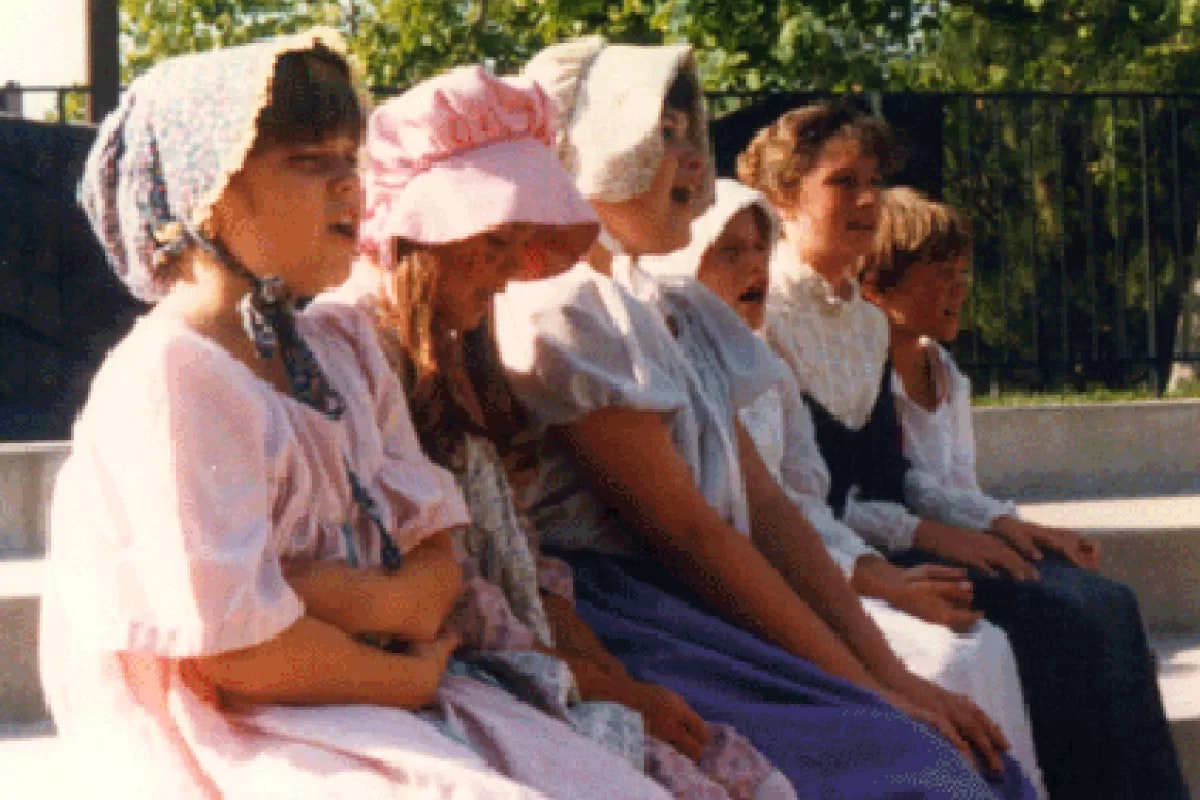 A group of people wearing pioneer-style clothing sitting in a row outdoors.