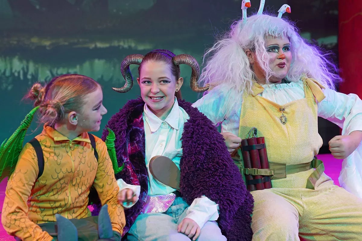 Three people in colorful fantasy costumes on stage, smiling.