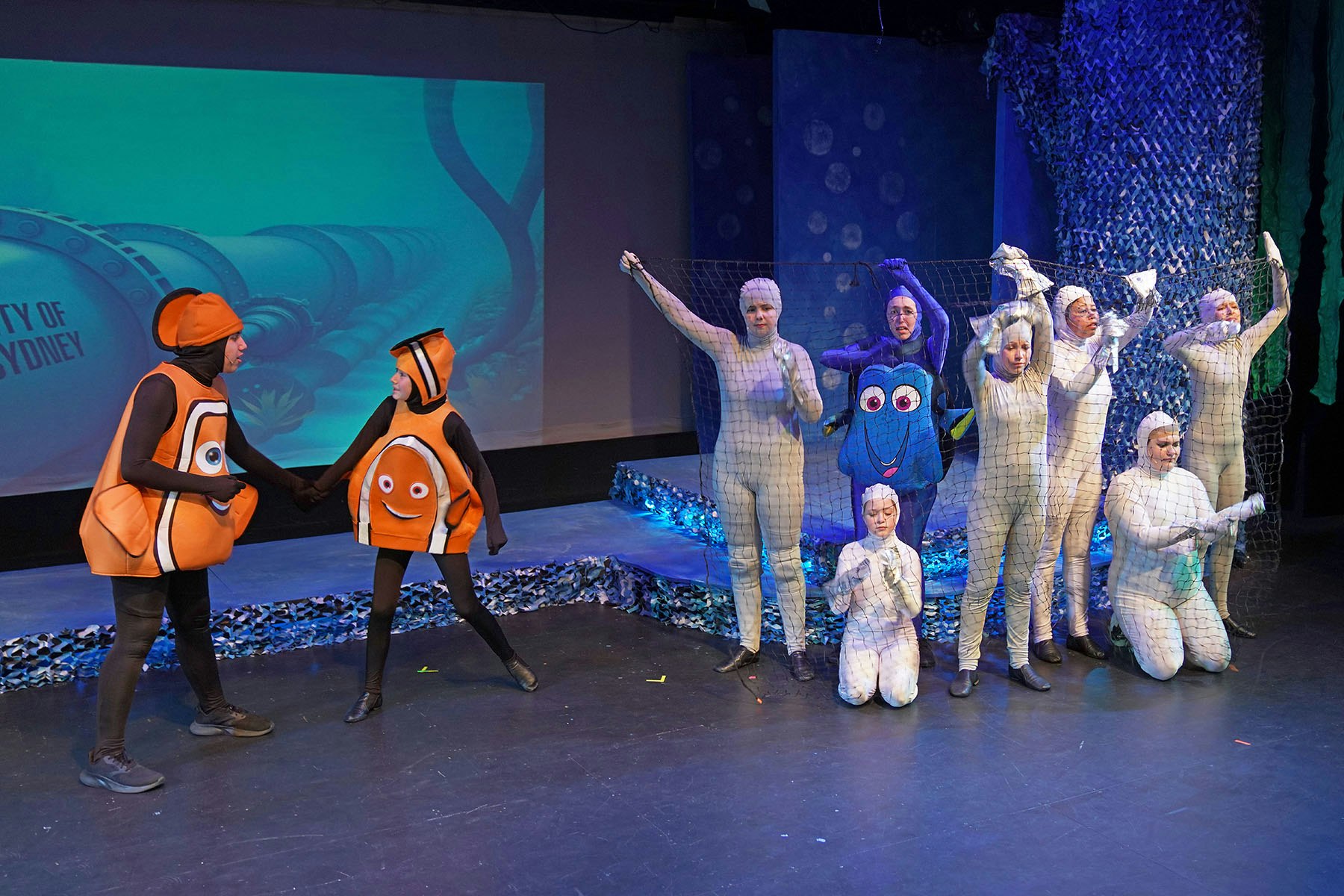 People in "Finding Nemo" costumes are performing on stage, with a backdrop screen and net-themed props.