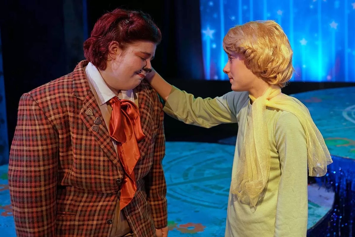 Two people in costumes are in a theater scene with a blue, starry background.