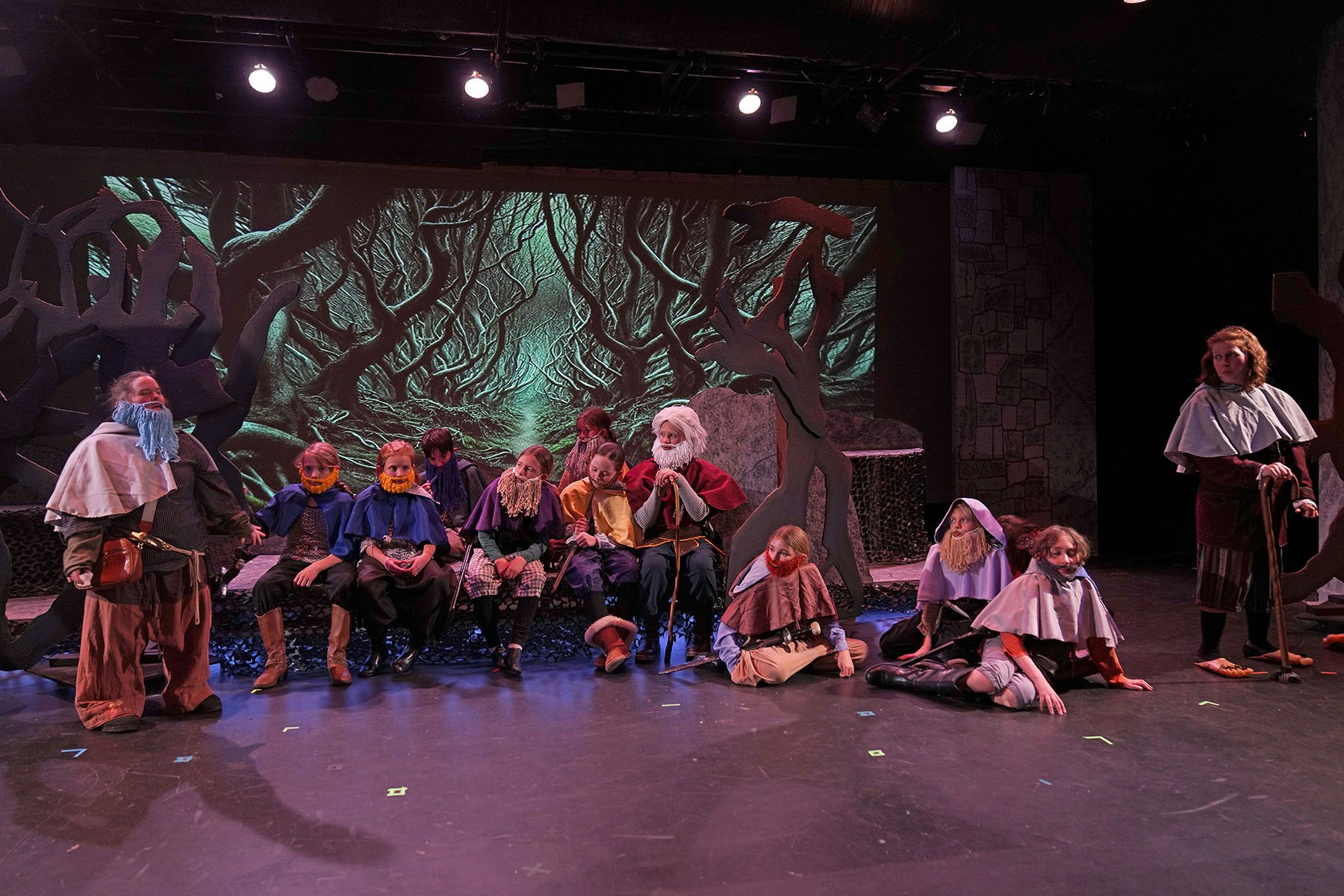 A theater production with actors in medieval costumes, set in a forest backdrop.